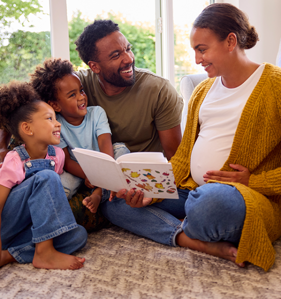 A pregnant mother reads a book to her two young children and her husband