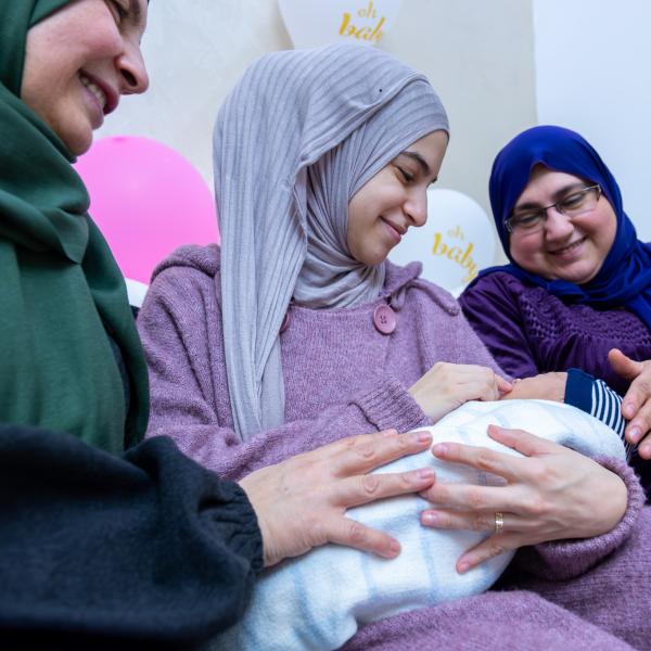 A new mother holds her newborn while her mother and sister watch the baby lovingly.