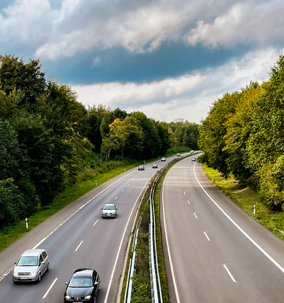 Cars drive on a four lane highway under a partially cloudy sky.