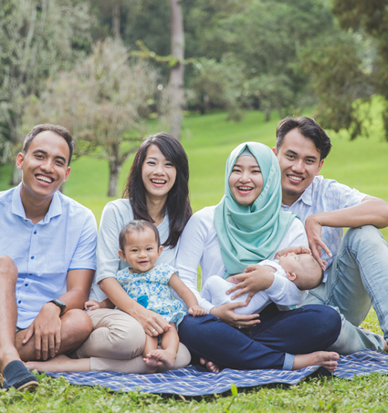 An extended family with two mothers and a young child and a newborn sit together at a picnic.