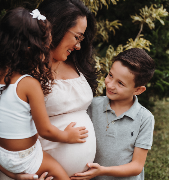 A pregnant mother stands laughing with her two children.